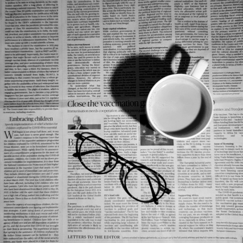 Open newspaper lying flat, with a cup and a pair of glasses on it.