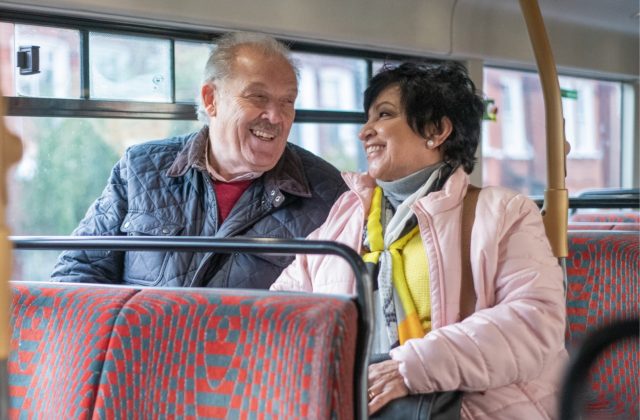 Two older people, sat together on top deck of a bus, laughing