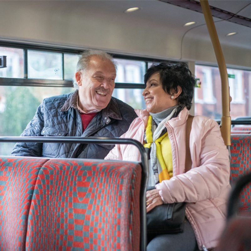 Two older people, sat together on top deck of a bus, laughing