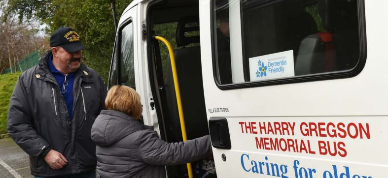 Woman getting on a white minibus, labelled 'The Harry Gregson Memorial bus'