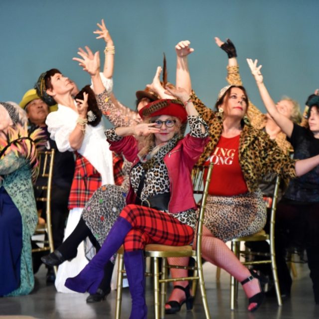 Group of brightly dressed older people holding a dance pose together