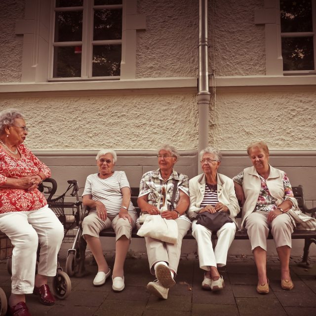 Group of older women sat together on a bench, with one in a wheelchair.