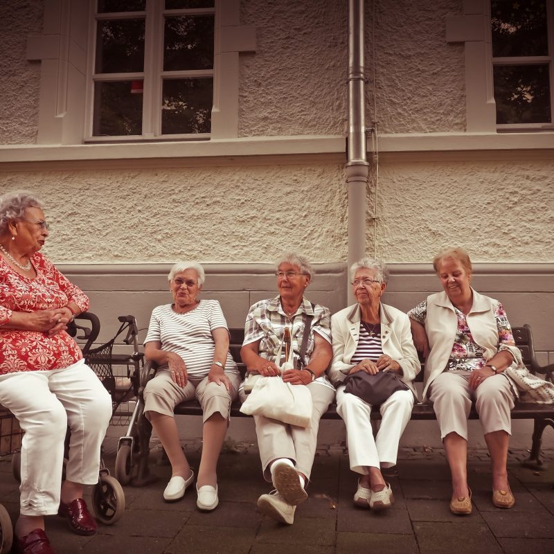 Group of older women sat together on a bench, with one in a wheelchair.