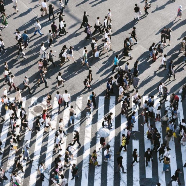 Lots of people, viewed from above, crossing main roads in an urban environment