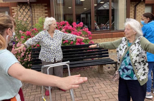 Older women, outside, with arms oustretched.