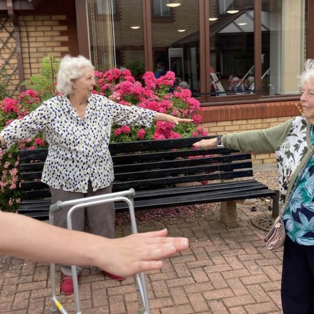 Older women, outside, with arms oustretched.