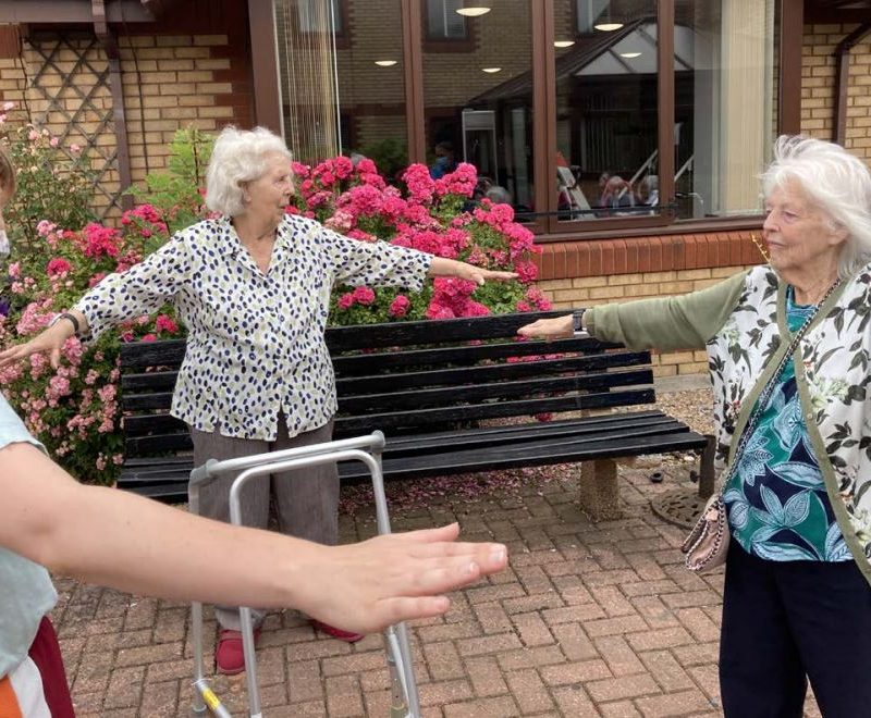 Older women, outside, with arms oustretched.