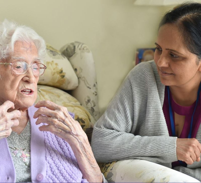 Older woman talking, with younger woman, leaning close, listening