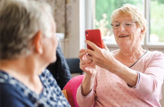 One older woman taking a photo of another, on a mobile phone.