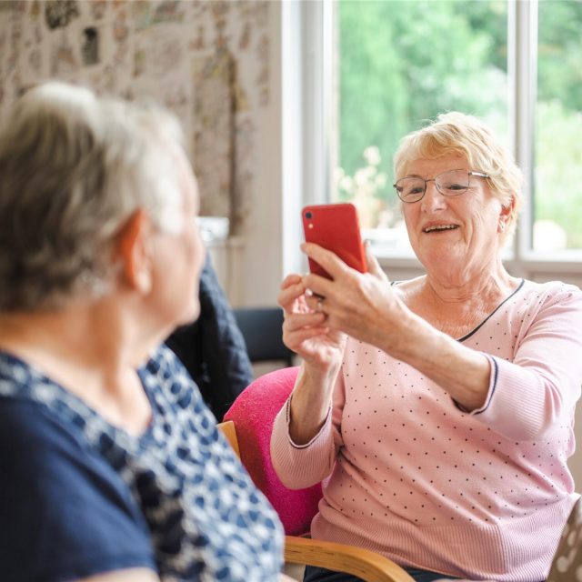 One older woman taking a photo of another, on a mobile phone.