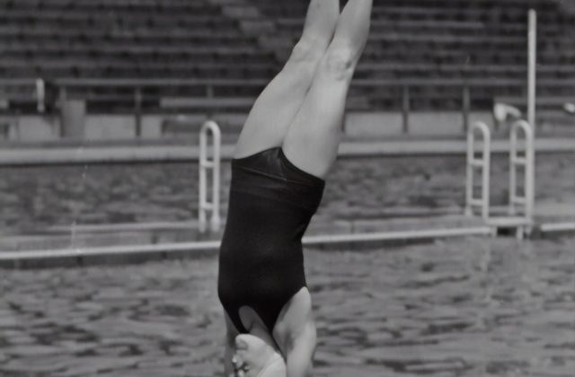 Woman in swimsuit about to enter the water, vertically, in a swimming pool.