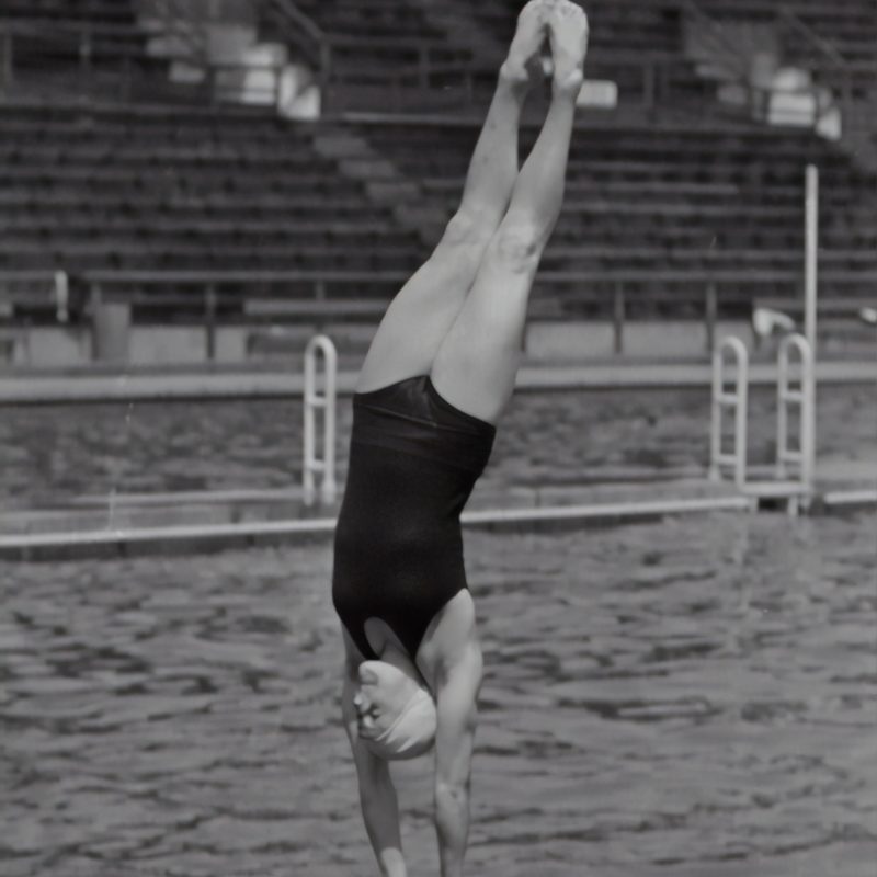 Woman in swimsuit about to enter the water, vertically, in a swimming pool.