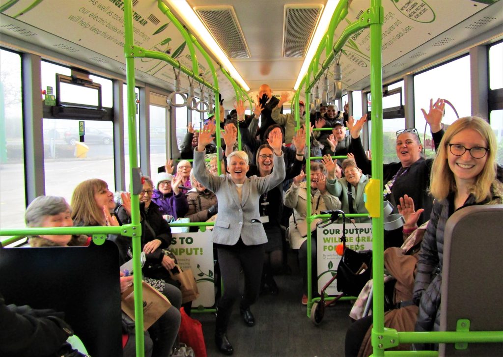 Lots of people inside a bus, waving straight at the camera