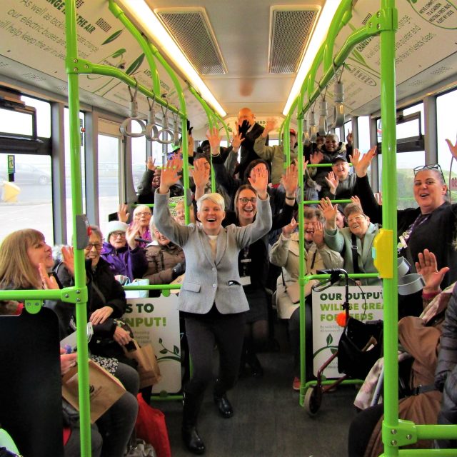 Lots of people inside a bus, waving straight at the camera