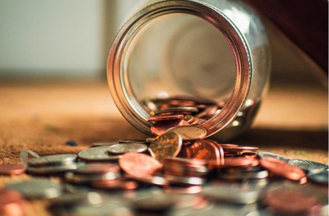 Glass jar lying on its side with loads of coins pouring out of it