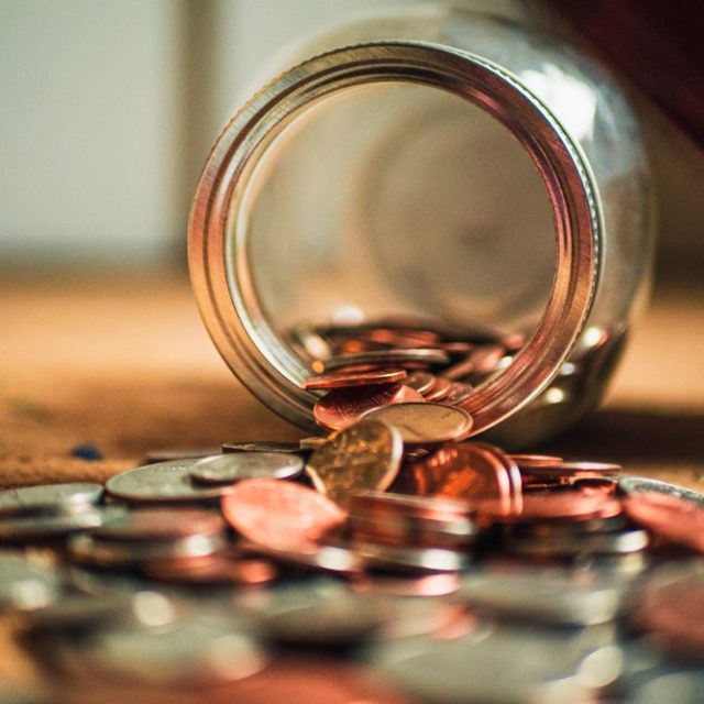 Glass jar lying on its side with loads of coins pouring out of it