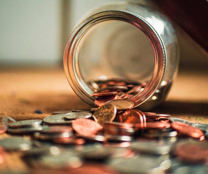 Glass jar lying on its side with loads of coins pouring out of it