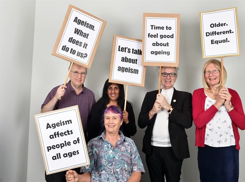 5 people each holding a placard, which say: "Let's talk about ageism", "Ageism. What does it do to us?", "Time to feel good about ageing", "Older. Different. Equal.", "Ageism affects people of all ages."