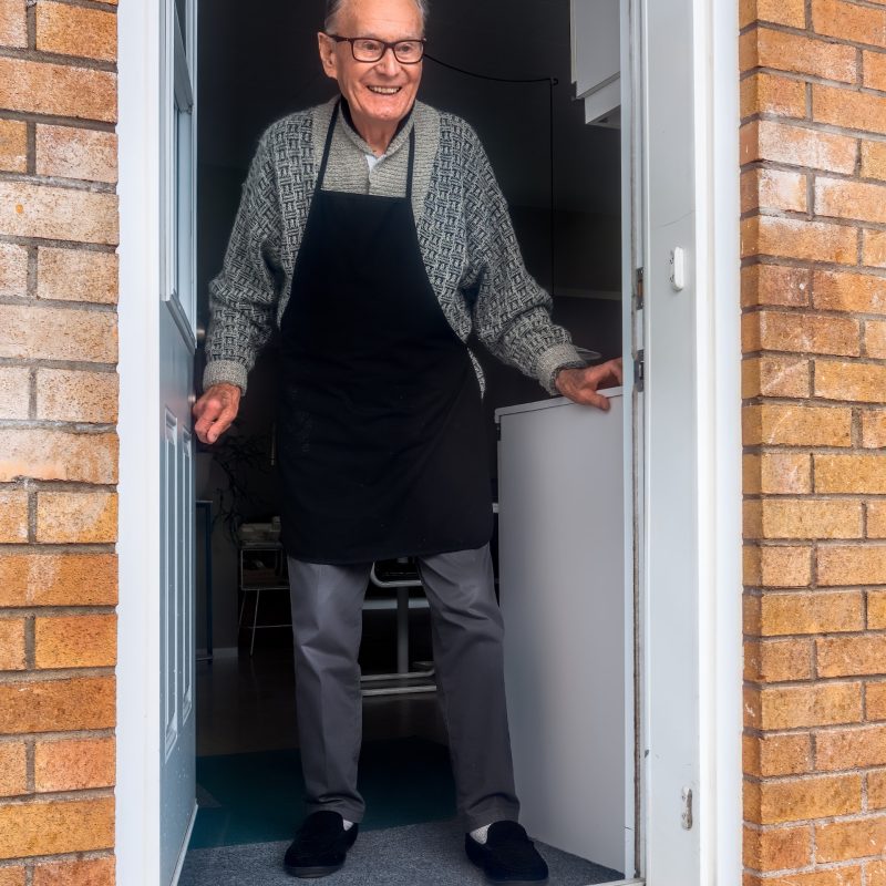 Older man at open door, smiling, with a small package in front of him