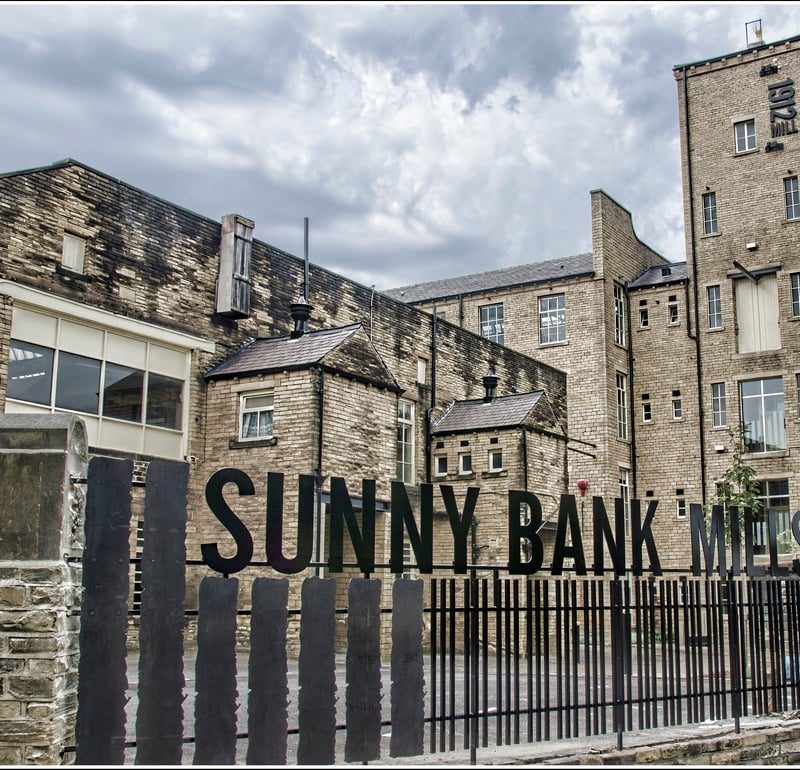 Large building, typical of northern England mill towns, with large sign "Sunny Bank Mills "