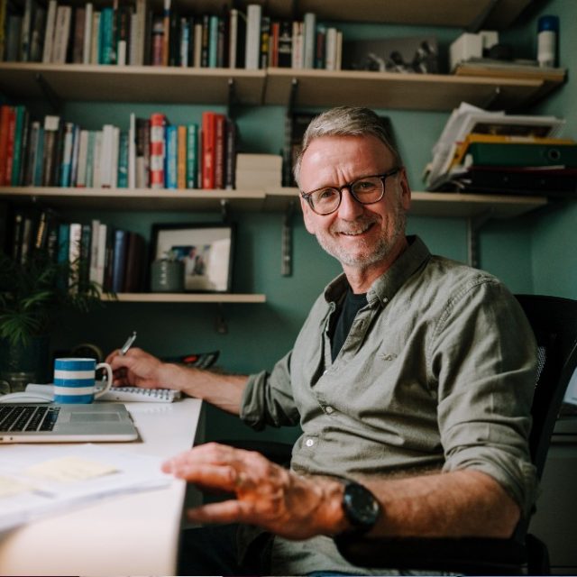 Photo image of a man using a laptop and smiling at the camera