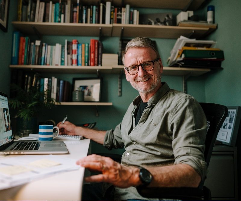 Photo image of a man using a laptop and smiling at the camera